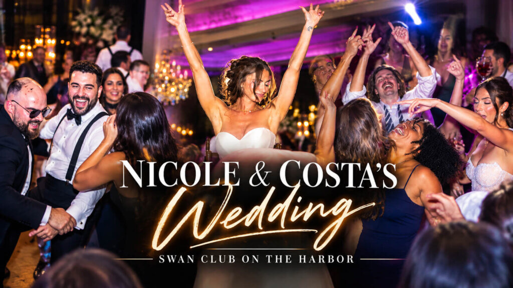Bride Nicole celebrates with her arms raised above a packed dance floor as wedding guests dance and cheer at Swan Club on the Harbor in Roslyn, NY, with DJ entertainment by DJ Taso.